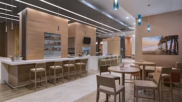 A modern bar area with a long counter, multiple bar stools, and a television mounted on the wall.