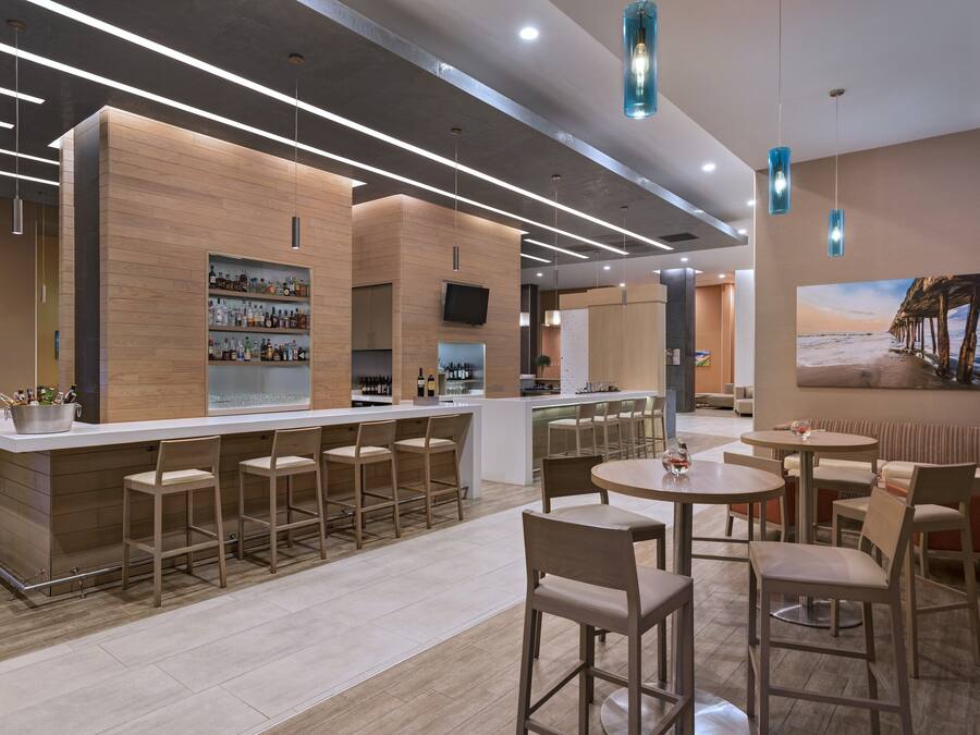 A modern bar area with a long counter, multiple bar stools, and a television mounted on the wall.