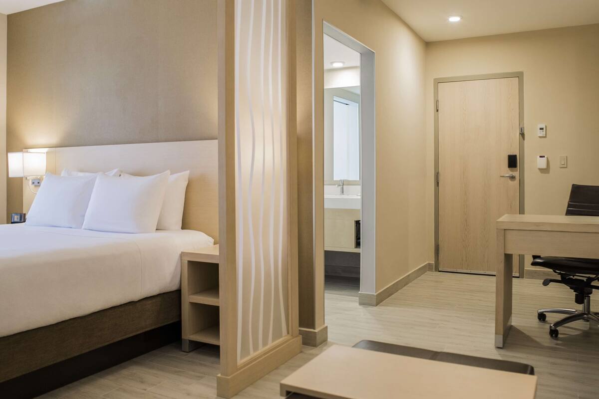 A hotel room with a bed, a desk, a chair, and a bathroom visible through an open door.