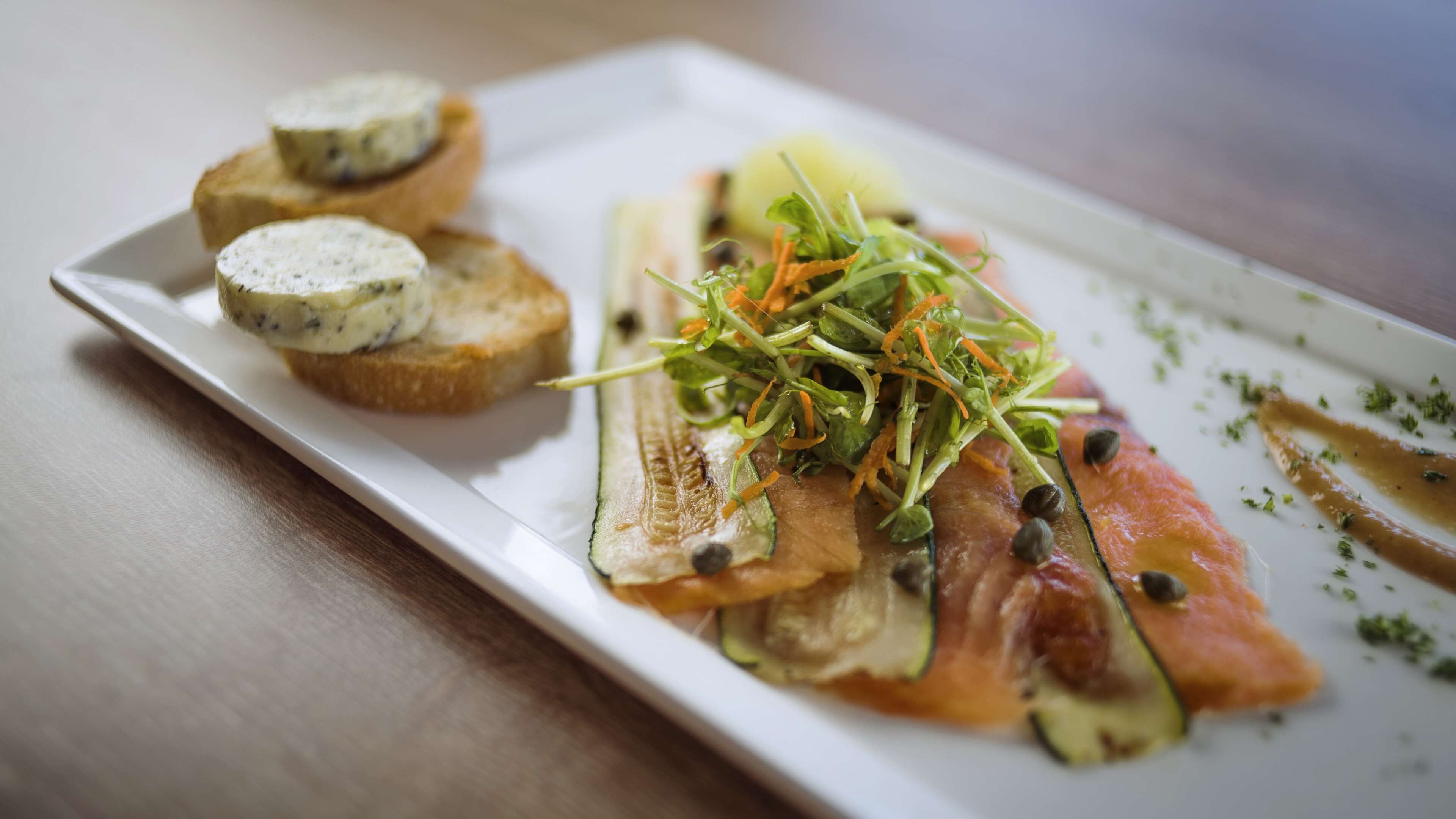 A plate with smoked salmon, cucumber, and a garnish of greens and carrots.