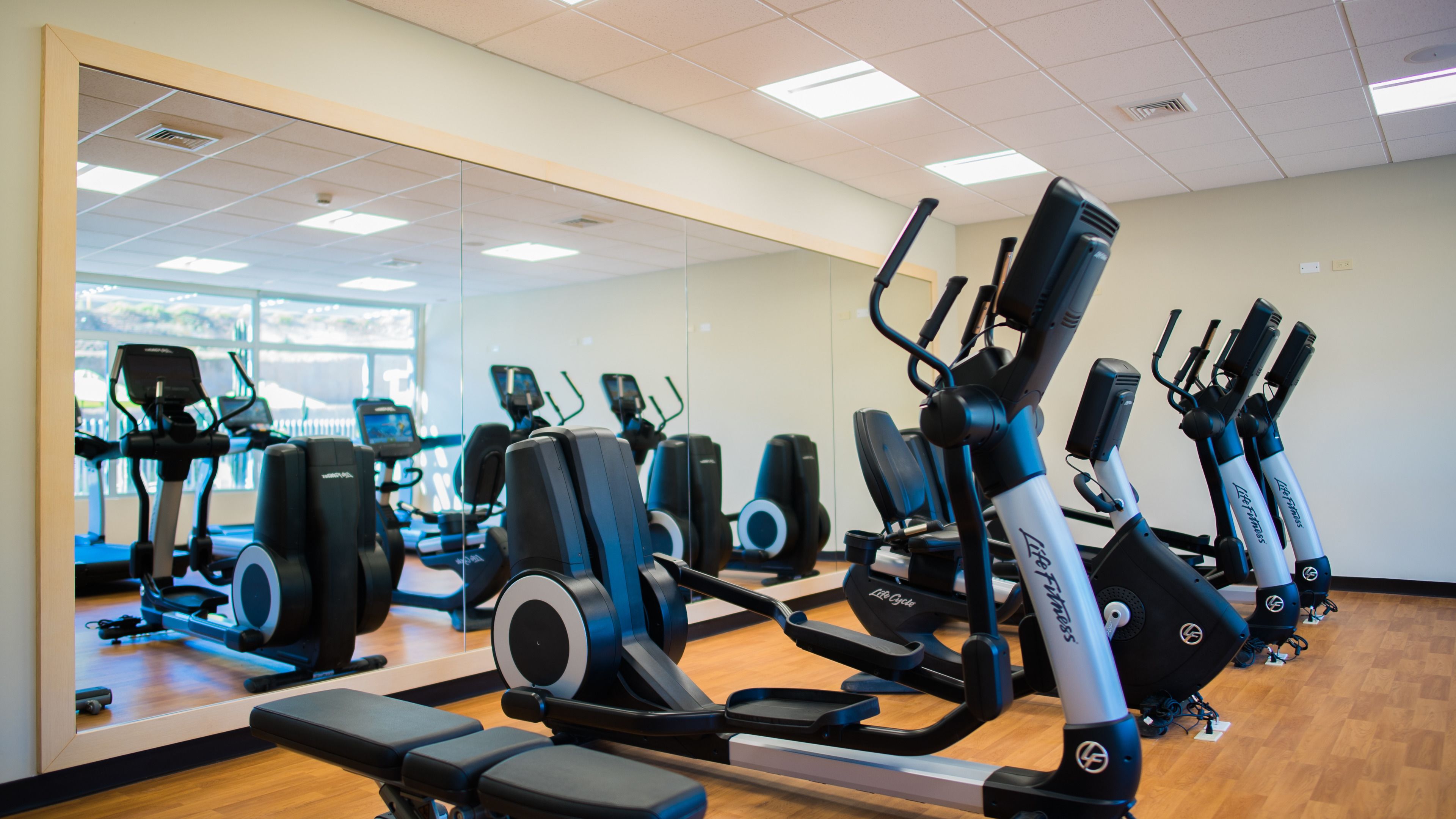 Une salle de sport équipée de matériel d’exercice, dotée d’un grand miroir et d’un plancher en bois.