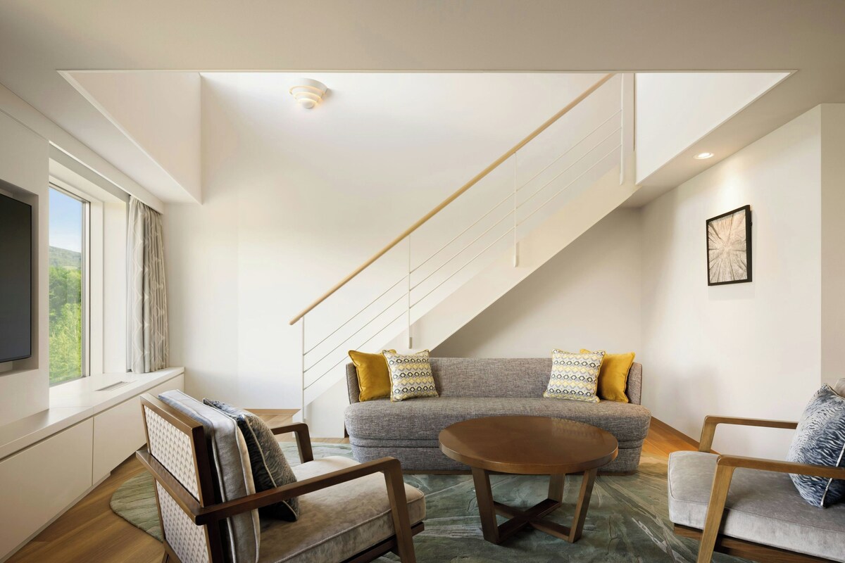 A modern living room with a sofa, armchairs, a coffee table, and a staircase.