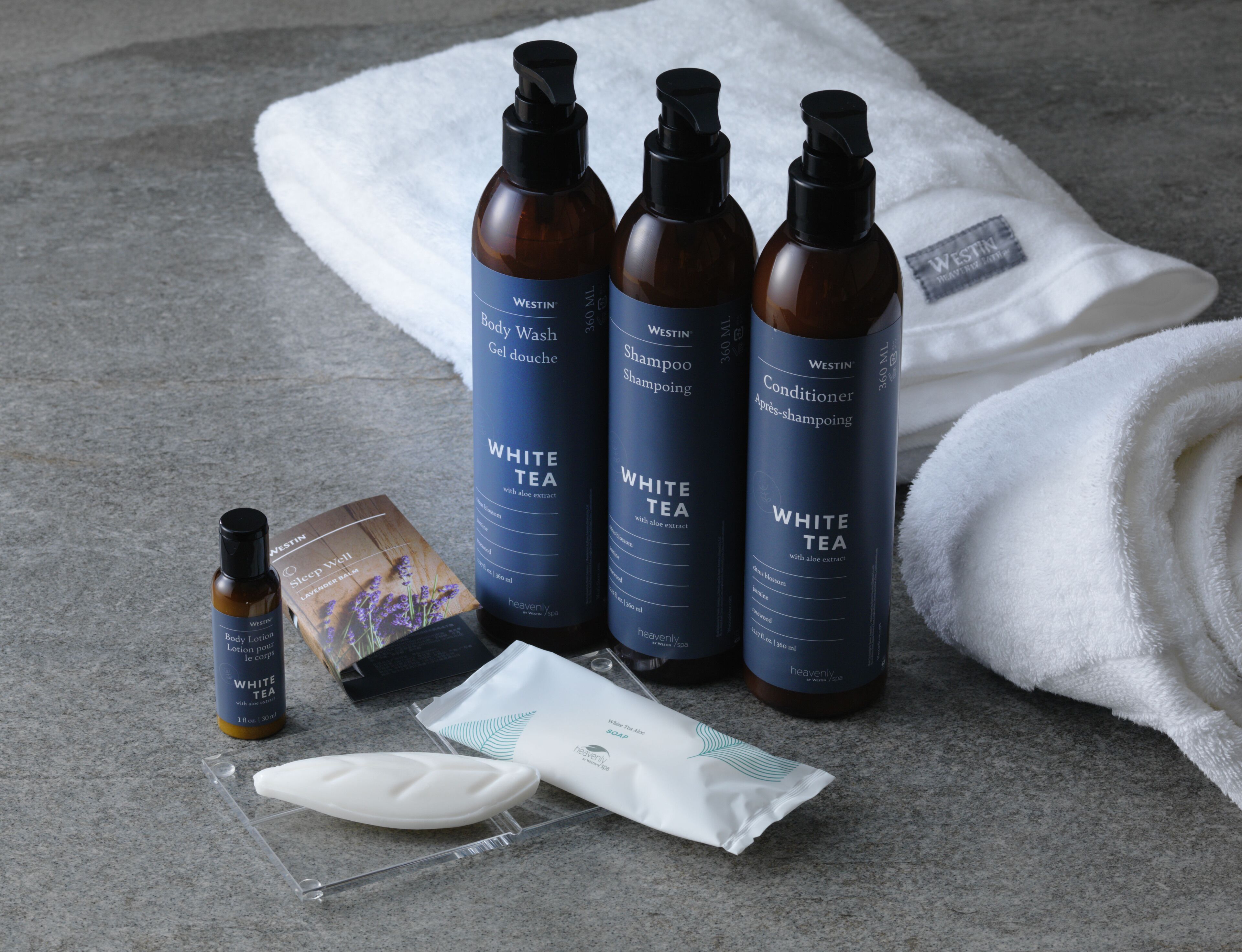 A set of Westin toiletries including body wash, shampoo, conditioner, and a body lotion, along with a white towel and a small bottle of white tea.