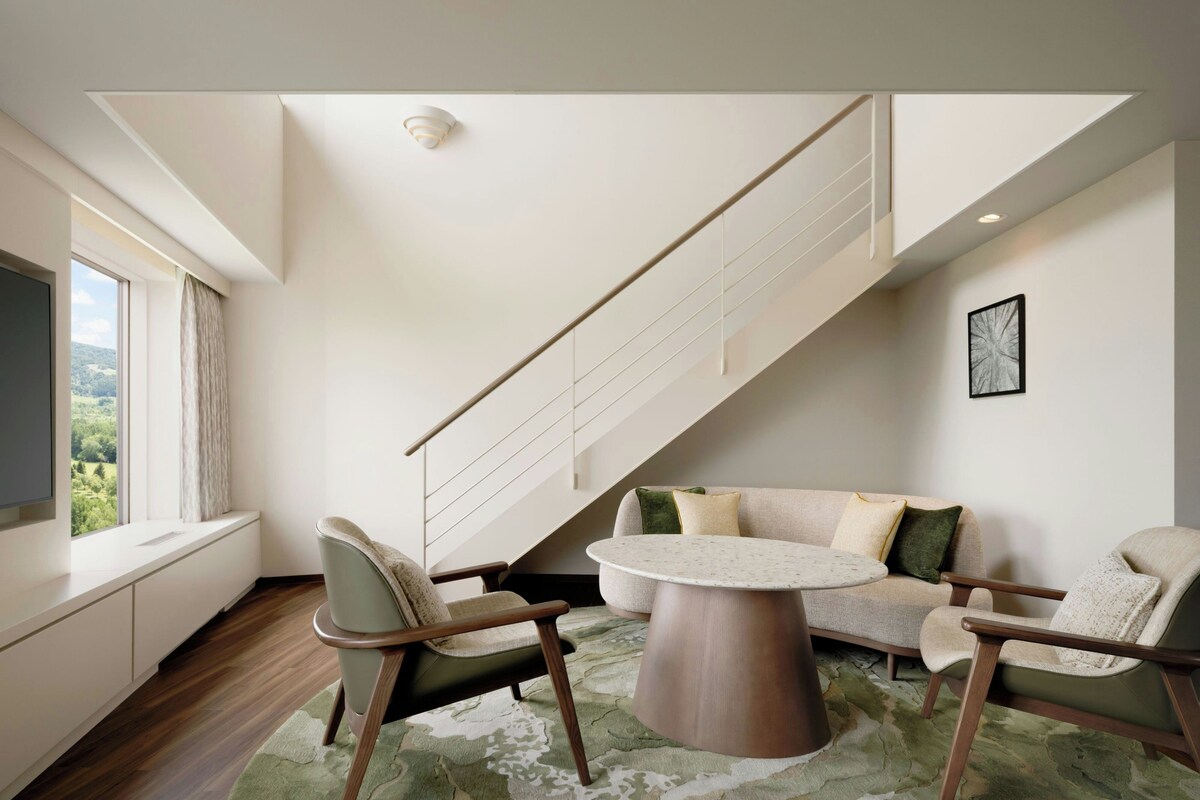 A modern living room with a staircase, a round table, and two chairs.