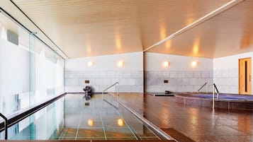 Relax and unwind in our indoor pool area, featuring a sleek, rectangular pool with clear glass sides and a polished stone floor.