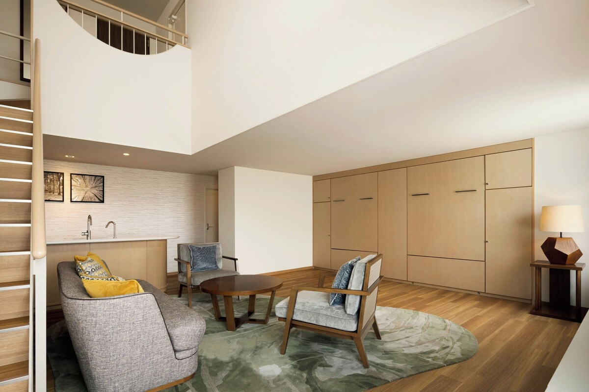 A modern living room with a sofa, chairs, a coffee table, and a kitchen area with a sink and cabinets.