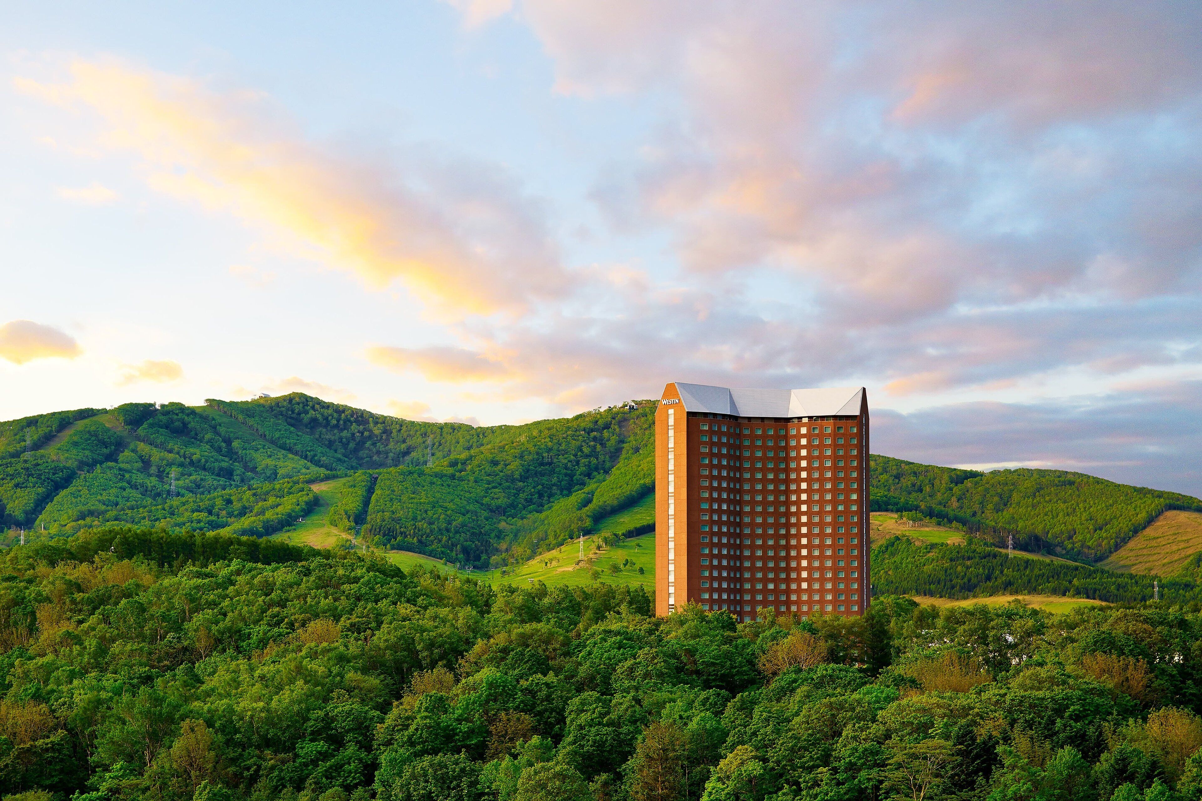 Un alto edificio de hotel con diseño moderno, rodeado de verdes colinas y un cielo despejado.