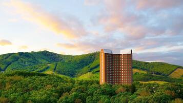 Un alto edificio de hotel con diseño moderno, rodeado de verdes colinas y un cielo despejado.