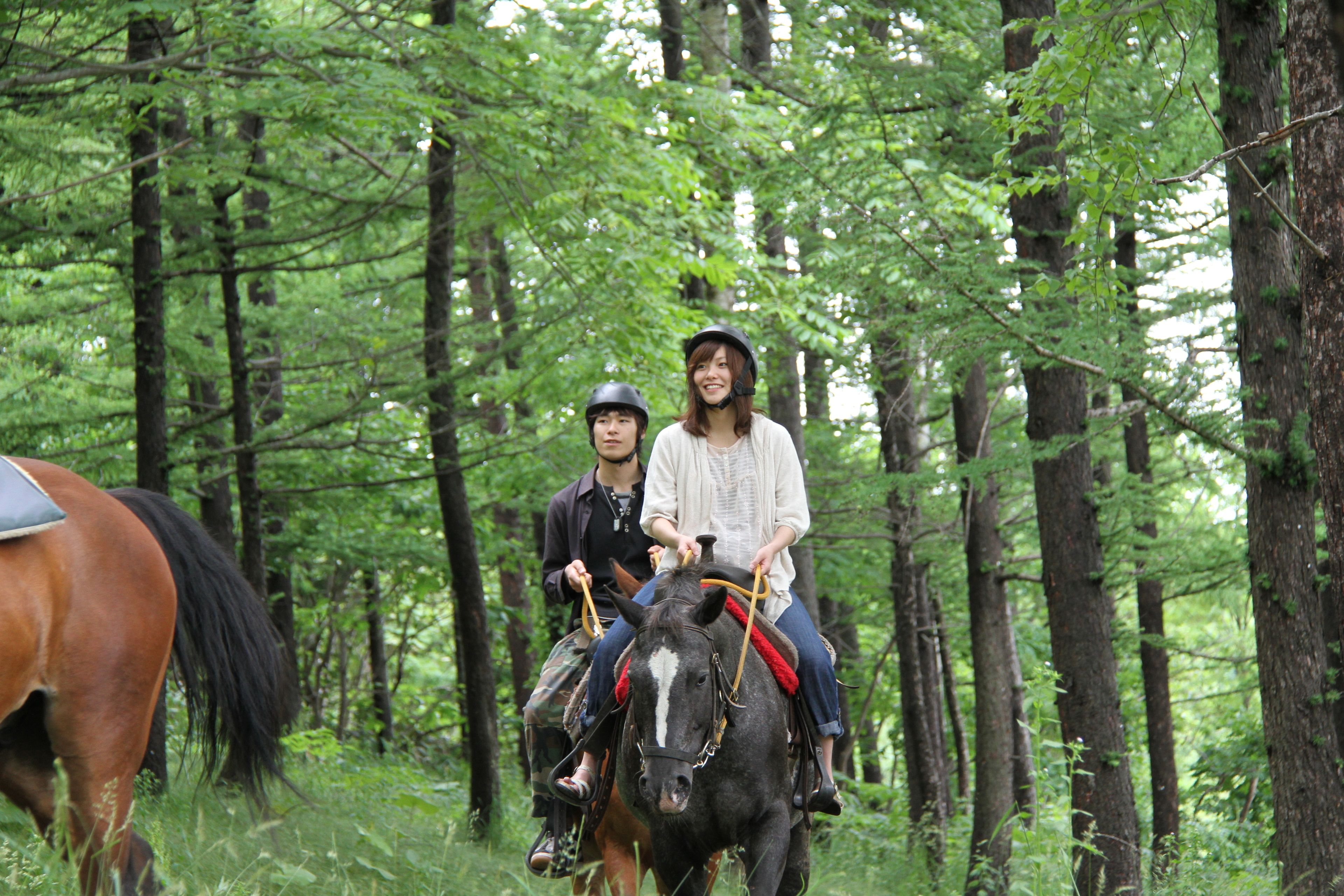 Deux personnes montent à cheval à travers une zone boisée.