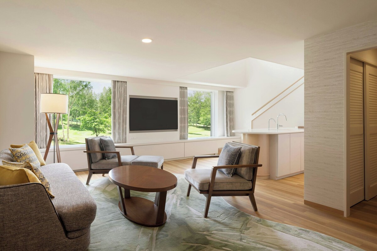 A modern living room with a flat-screen TV, comfortable seating, a dining area, and a view of the outdoors.