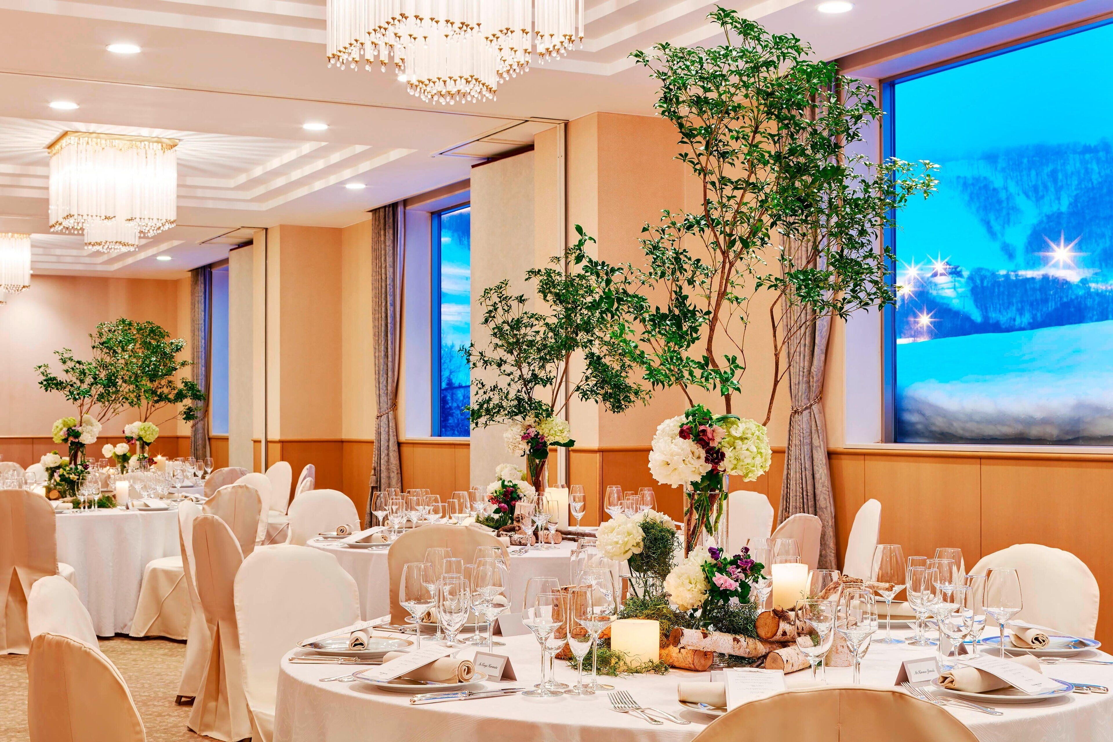 Ein Festsaal mit runden Tischen, festlich für eine Veranstaltung dekoriert mit Blumenarrangements und Kerzen.