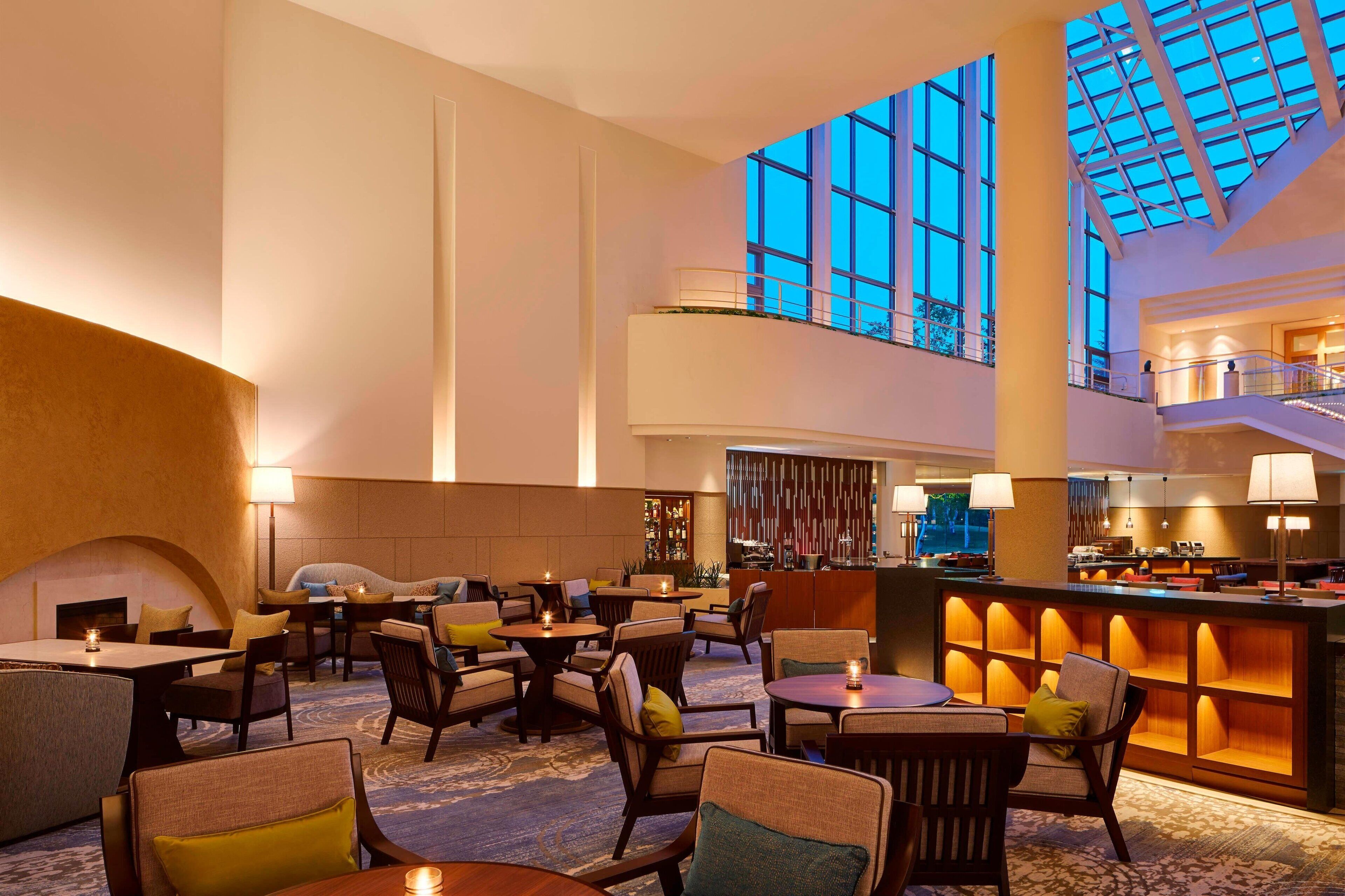 Un'ampia hall dell'hotel con diverse zone salotto, un bar centrale e grandi finestre che lasciano entrare la luce naturale.