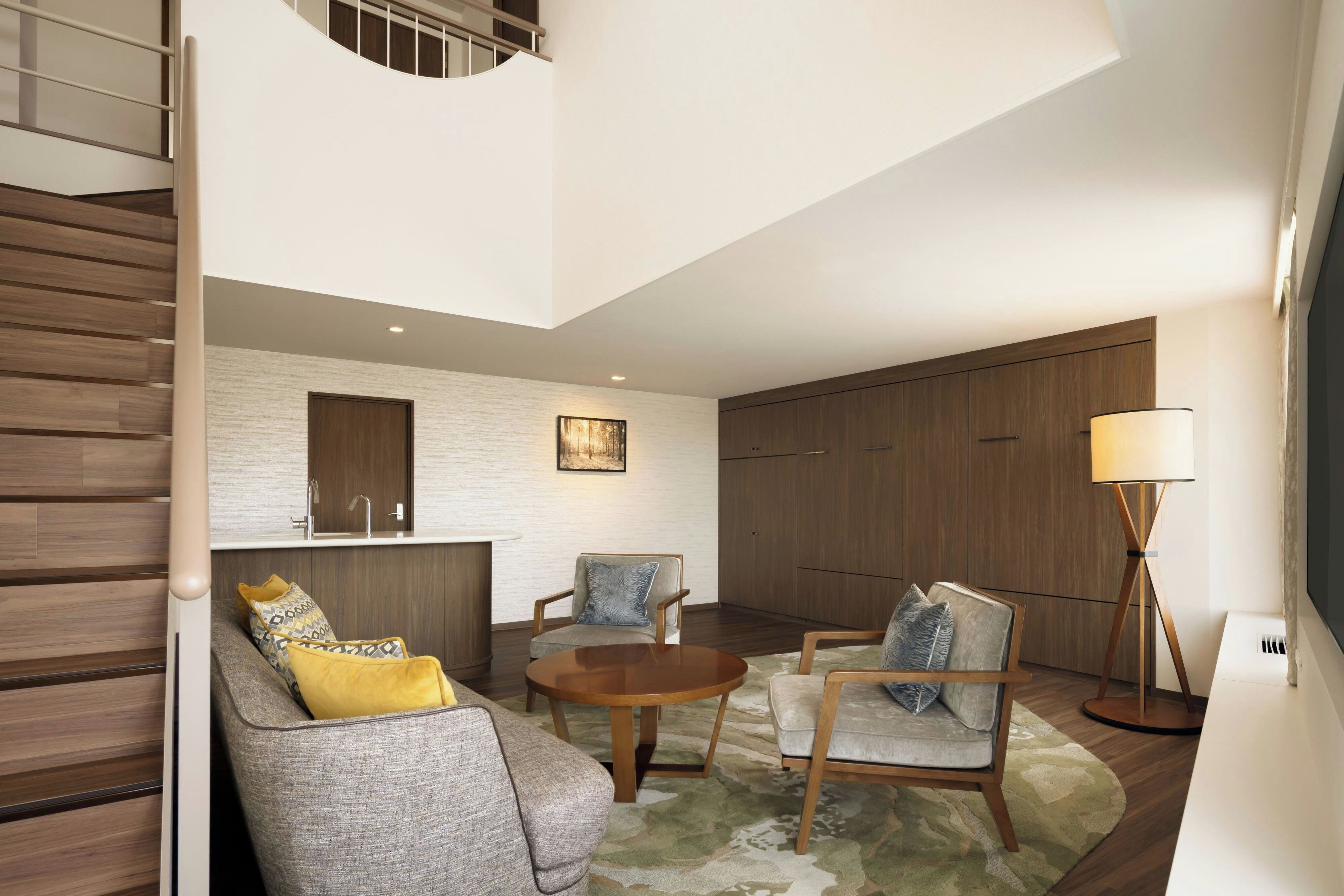 A modern living room with a staircase, a round wooden coffee table, and a sofa with patterned cushions.