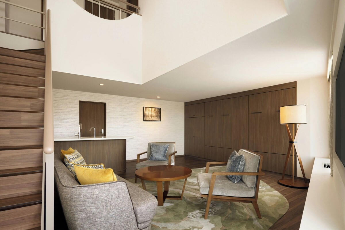 A modern living room with a staircase, a round wooden coffee table, and a sofa with patterned cushions.