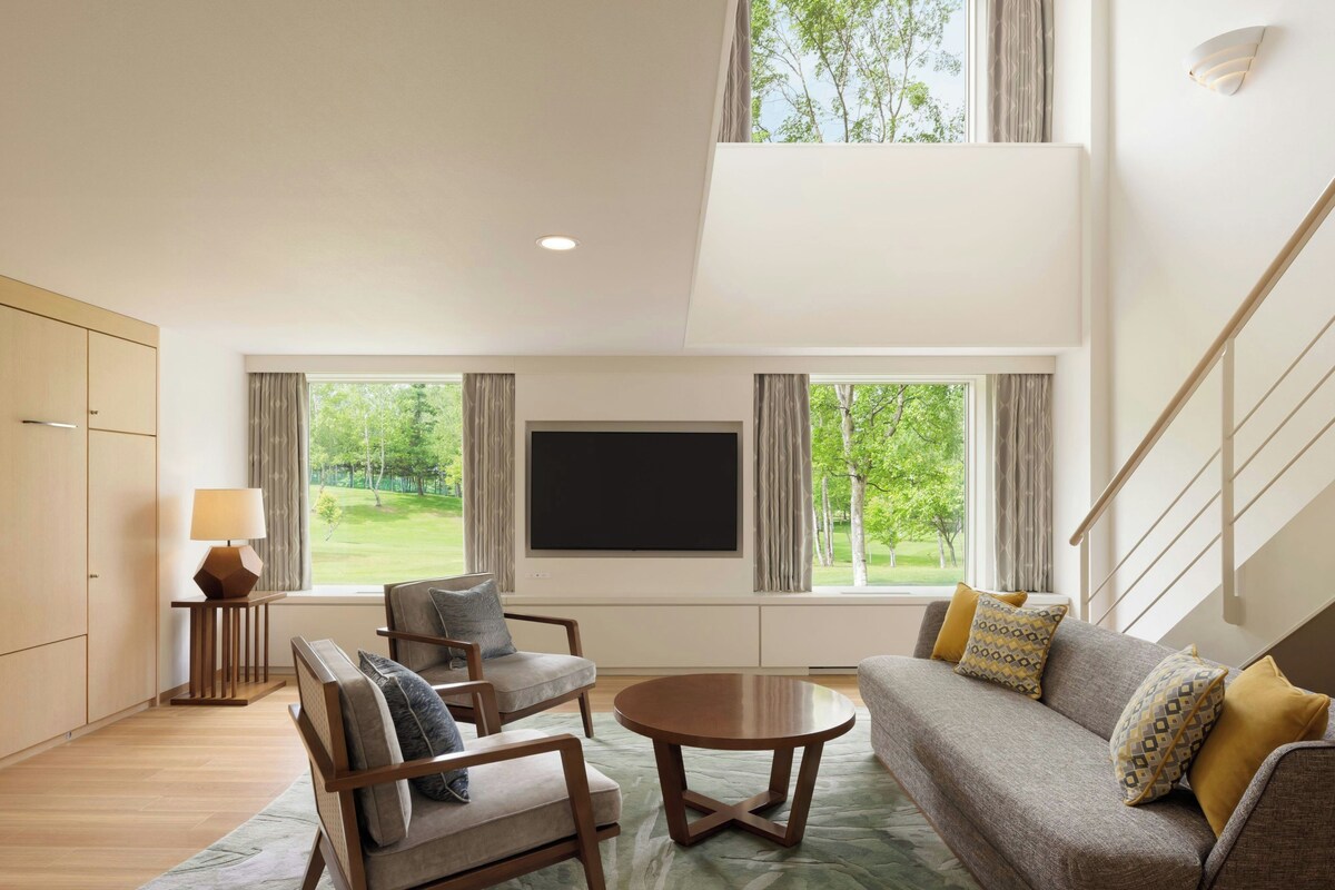 A modern living room with a flat-screen TV, two sofas, a coffee table, and a lamp.