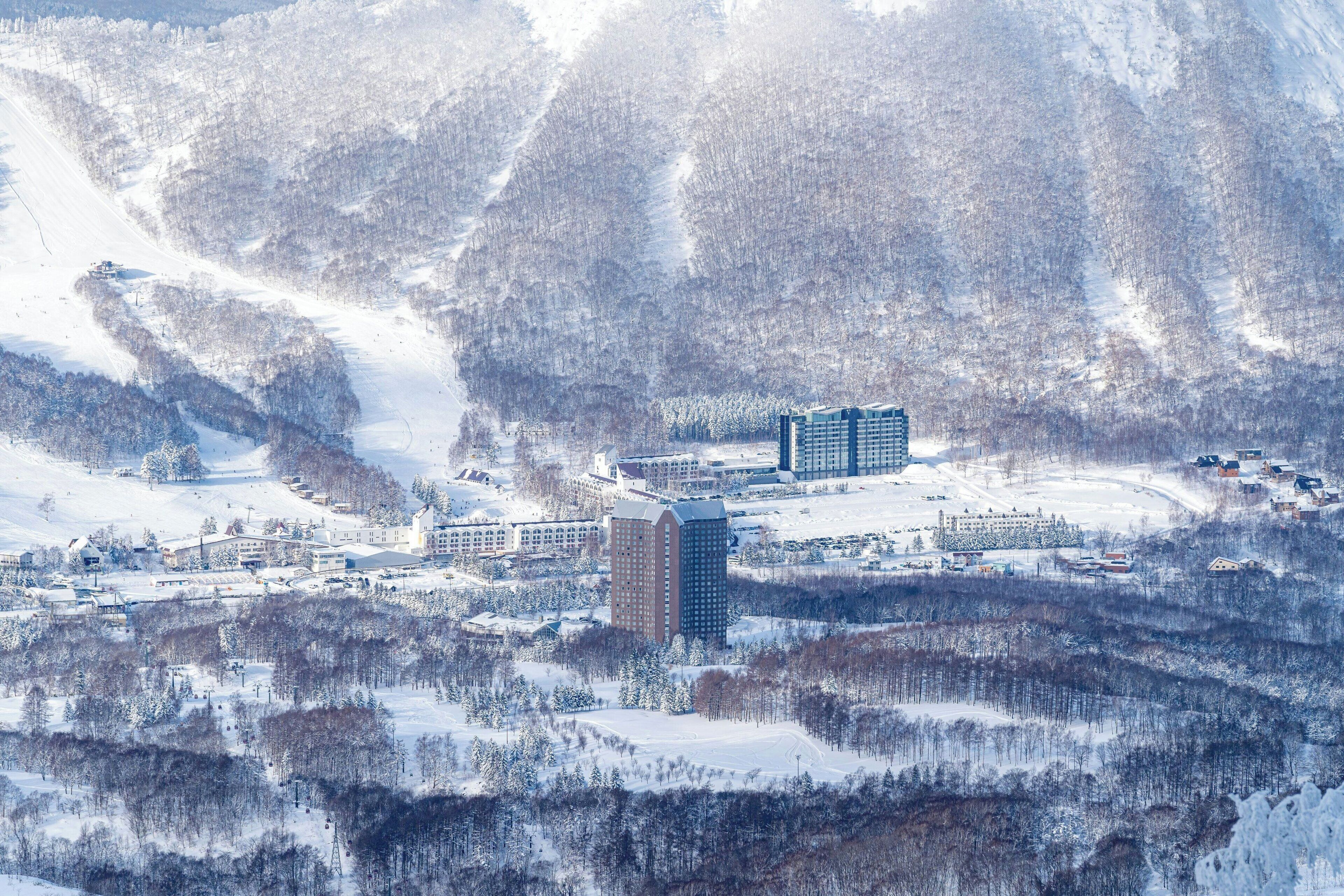 A snow-covered mountainous area with a large hotel complex featuring multiple buildings, including a prominent tall structure.