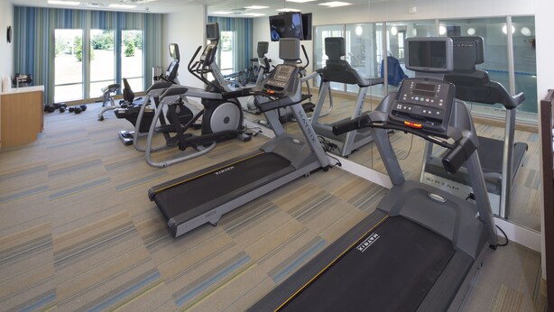 Un gimnasio con cintas de correr, bicicletas estáticas y un banco de pesas.