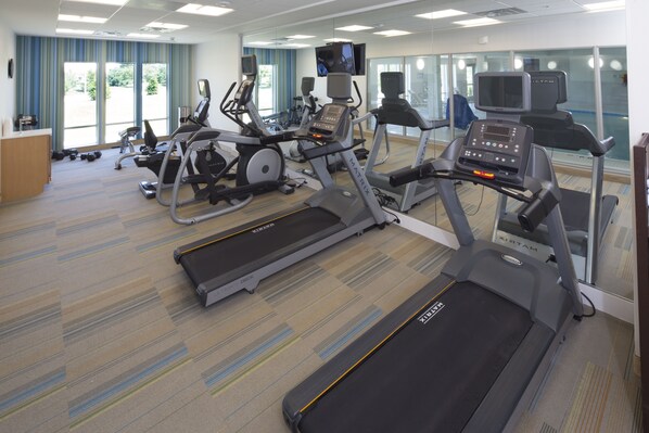 Un gimnasio con cintas de correr, bicicletas estáticas y un banco de pesas.