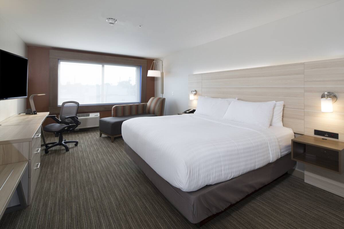 A modern hotel room with a large bed, a desk with a computer, a chair, and a TV.