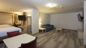 A hotel room with a bed, a desk, a chair, a sofa, a TV, and a lamp.
