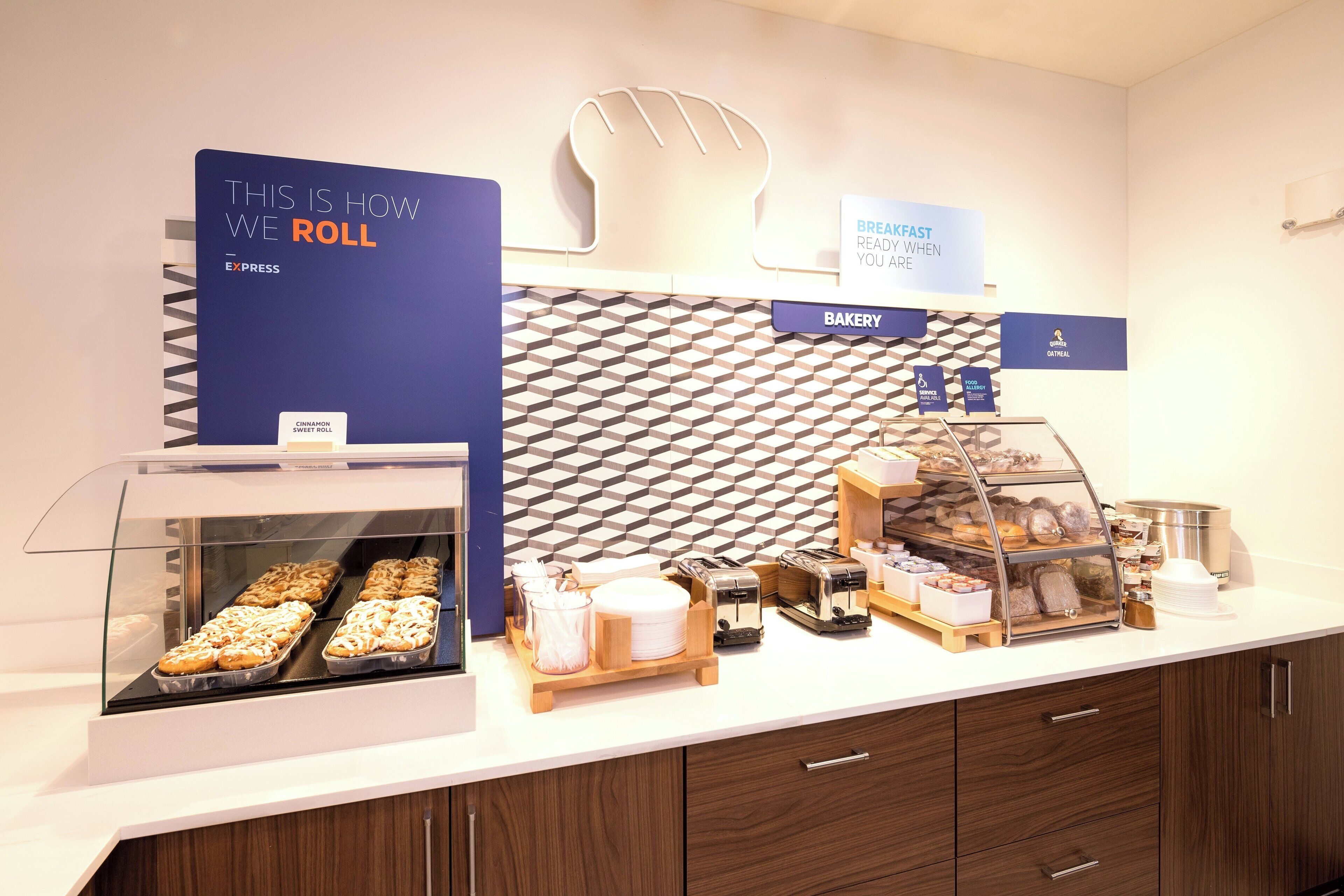 A bakery counter with a display of sweet rolls and a sign indicating breakfast is ready when you are.