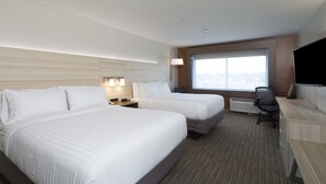 Habitación de hotel con dos camas, un escritorio, una silla, un televisor y una ventana con vista a la ciudad.