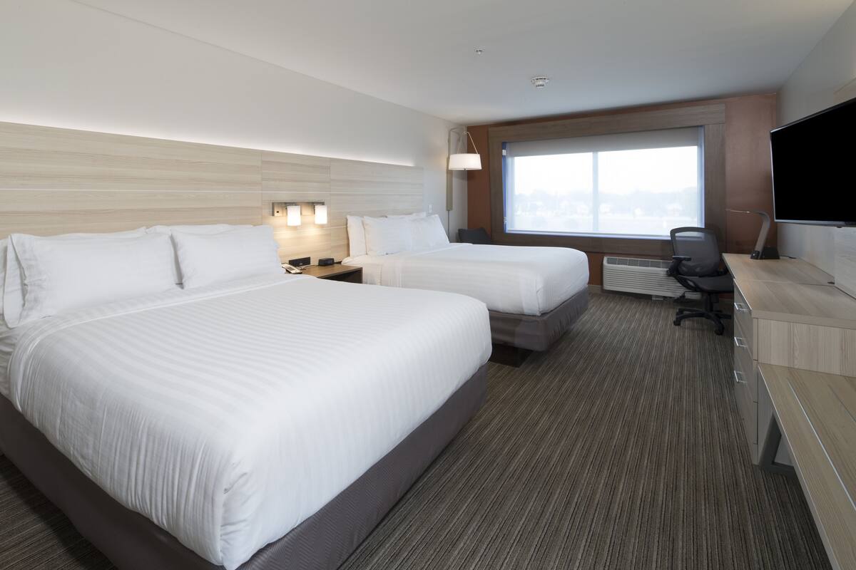 A hotel room with two beds, a desk, a chair, a TV, and a window with a city view.