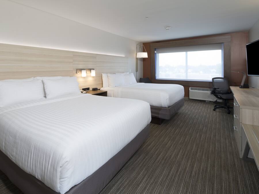 A hotel room with two beds, a desk, a chair, a TV, and a window with a city view.