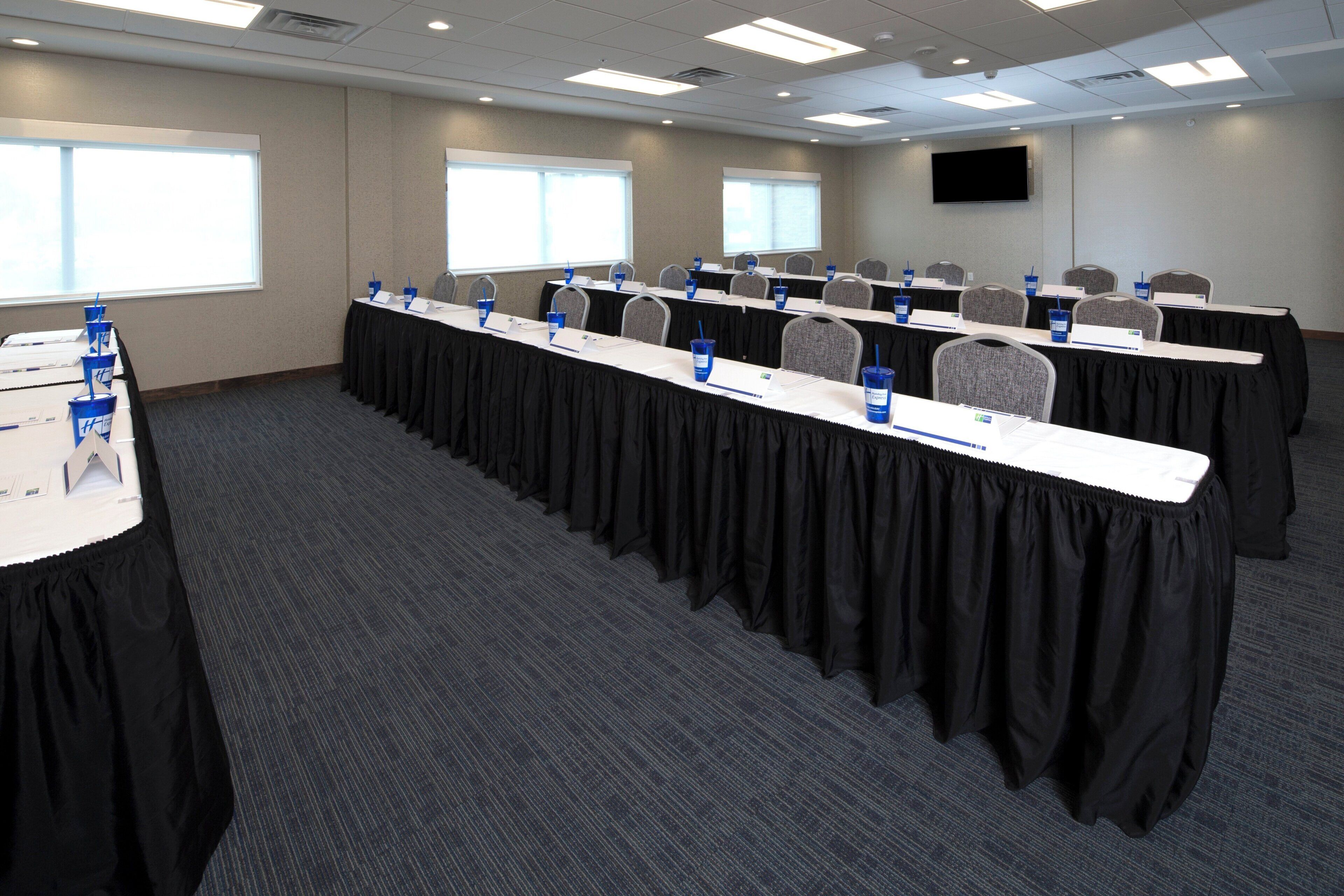Une salle de conférence avec des rangées de tables, des plaques nominatives et des bouteilles d’eau.