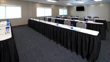 Une salle de conférence avec des rangées de tables, des plaques nominatives et des bouteilles d’eau.