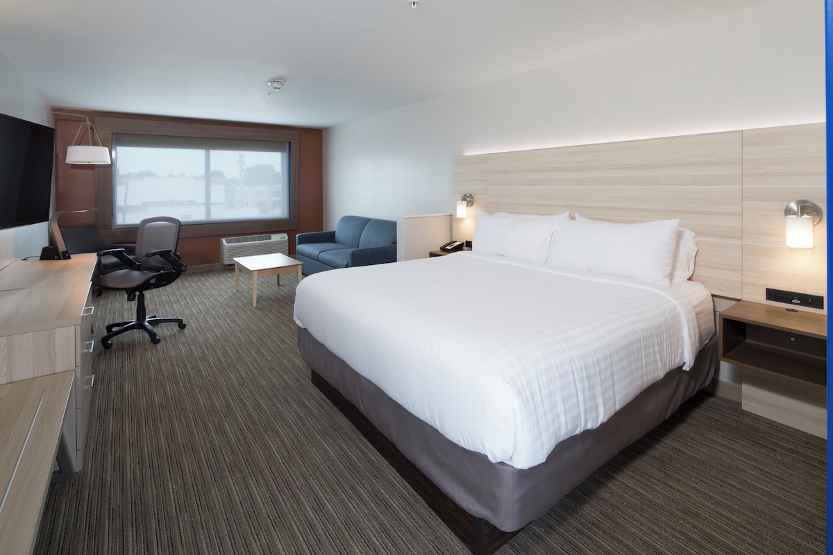 Habitación de hotel con una cama grande, un escritorio con silla, una mesita, un televisor y una ventana con vistas.