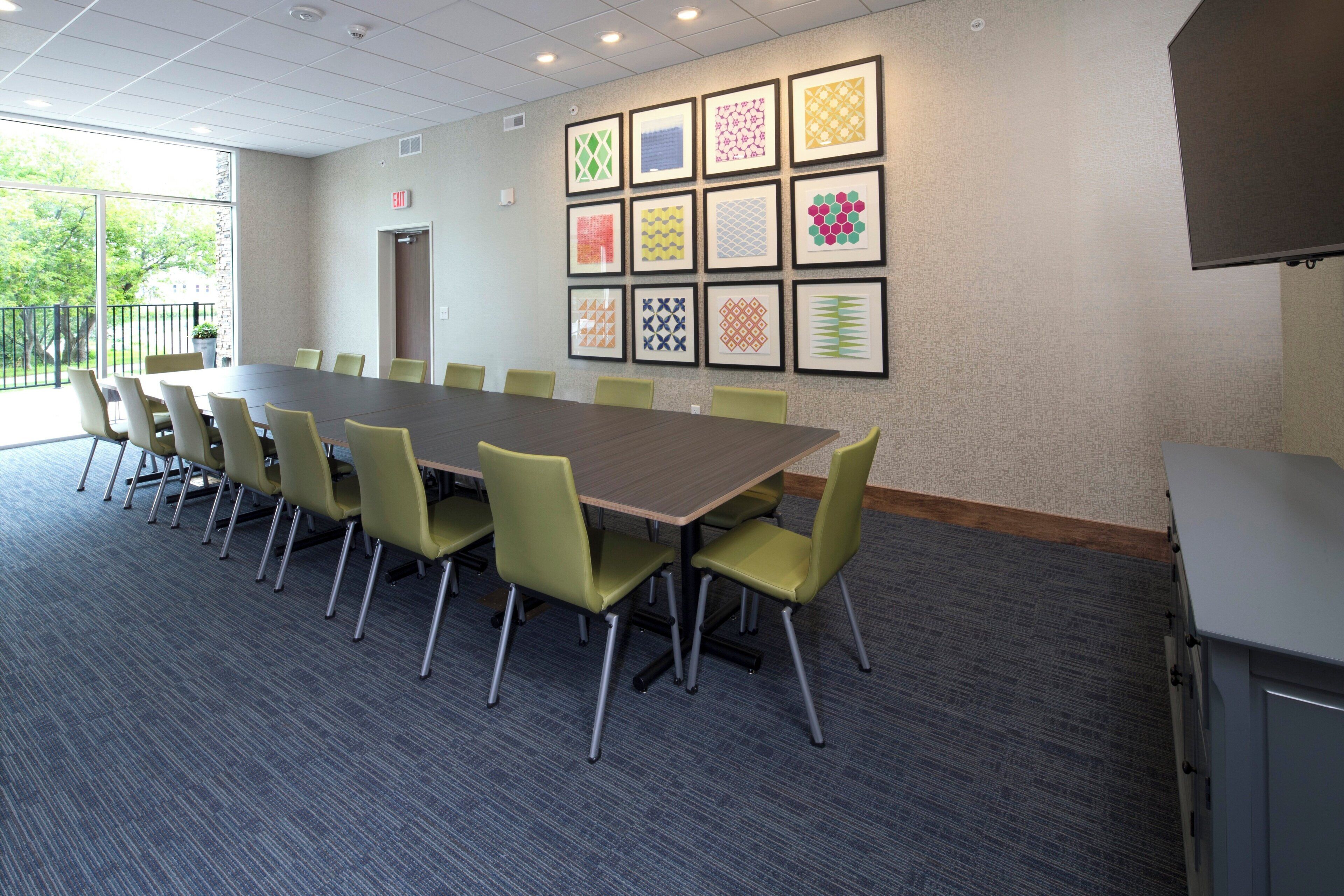 A conference room with a long table and chairs, a wall with framed geometric patterns, and a door.