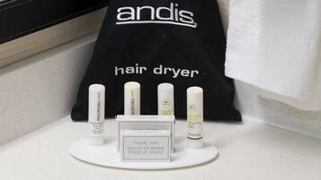 Una encimera de baño con una bolsa para secador de pelo, una pastilla facial y varios productos para el cabello.