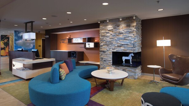 A modern lounge area with a stone fireplace, blue seating, and a flat-screen TV. - Fairfield Inn & Suites Houma Southeast (Houma)