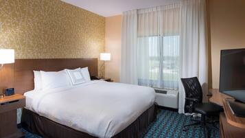 A hotel room with a large bed, a desk with a lamp, a chair, a TV, and a window with curtains.
