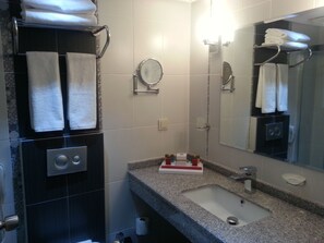 A bathroom with a sink, mirror, towel rack, and a small shelf with toiletries.