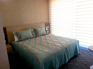 A hotel room with a bed, a nightstand, and a window with blinds.