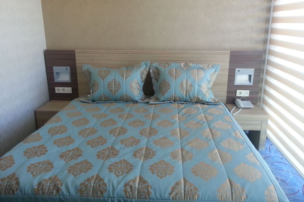 A bed with a patterned bedspread, two bedside tables with lamps, and a wall-mounted telephone.