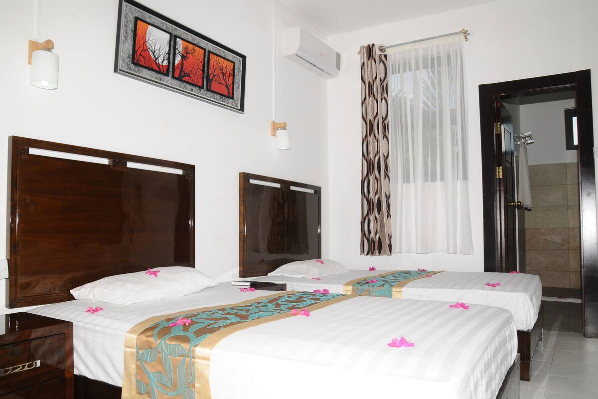 A hotel room with two beds, a wooden headboard, a mirror, a framed picture, a white lamp, and a shower area.