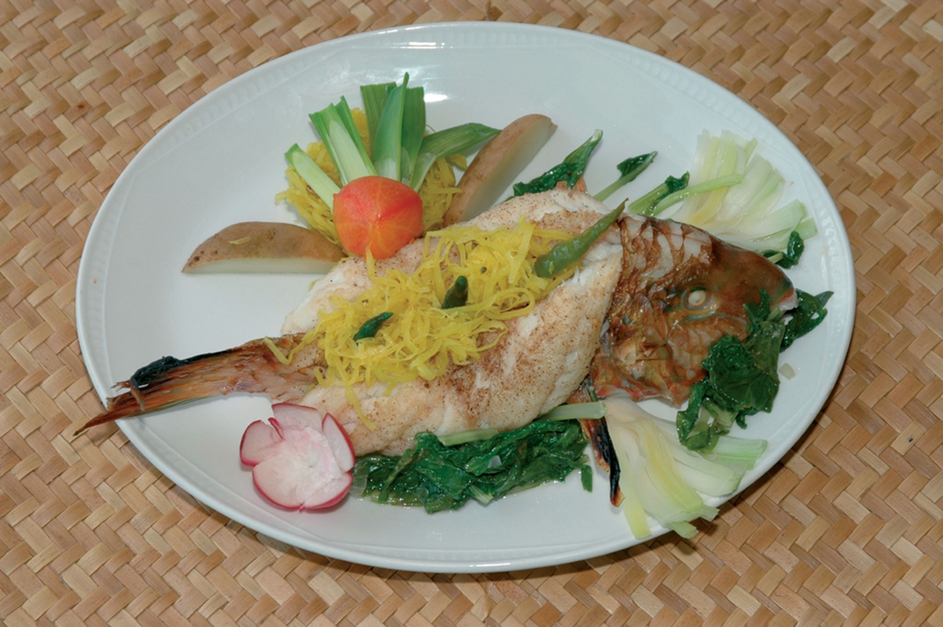 Un plato de comida con pescado, verduras y tomate.