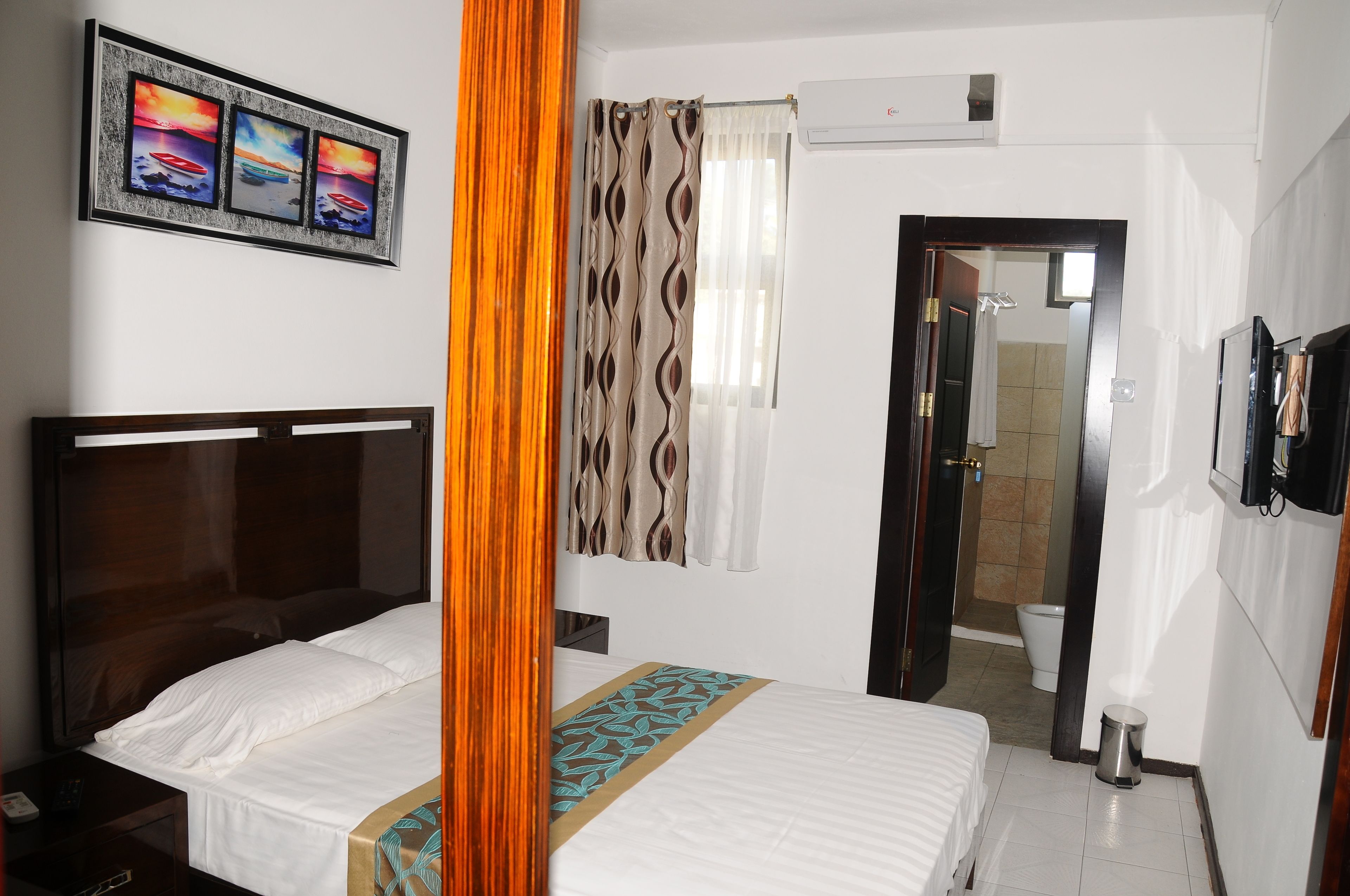A hotel room with a bed, a nightstand, a mirror, a framed picture on the wall, a shower area, and a toilet.