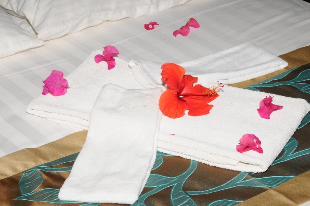 A neatly folded white towel with a hibiscus flower on a bed with a floral-patterned bedspread.