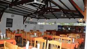 A restaurant with wooden tables and chairs, a bar area, and a high ceiling with exposed beams. - Le Flamboyant Hotel (Rodrigues Island)