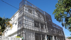 A multi-story building with a modern facade, featuring a series of vertical metal bars and a white exterior. - Le Flamboyant Hotel (Rodrigues Island)