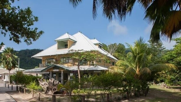 A two-story house with a sloped roof, surrounded by tropical vegetation and a clear sky. - Lakaz Safran (La Digue)
