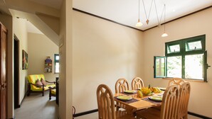 A dining area with a wooden table, chairs, and a window with green frames. - Lakaz Safran (La Digue)