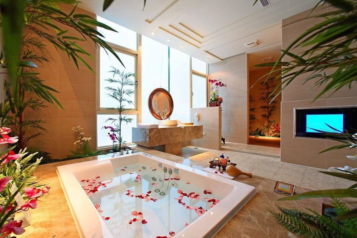 A modern bathroom with a large bathtub, a vanity with a mirror, and a television on the wall.