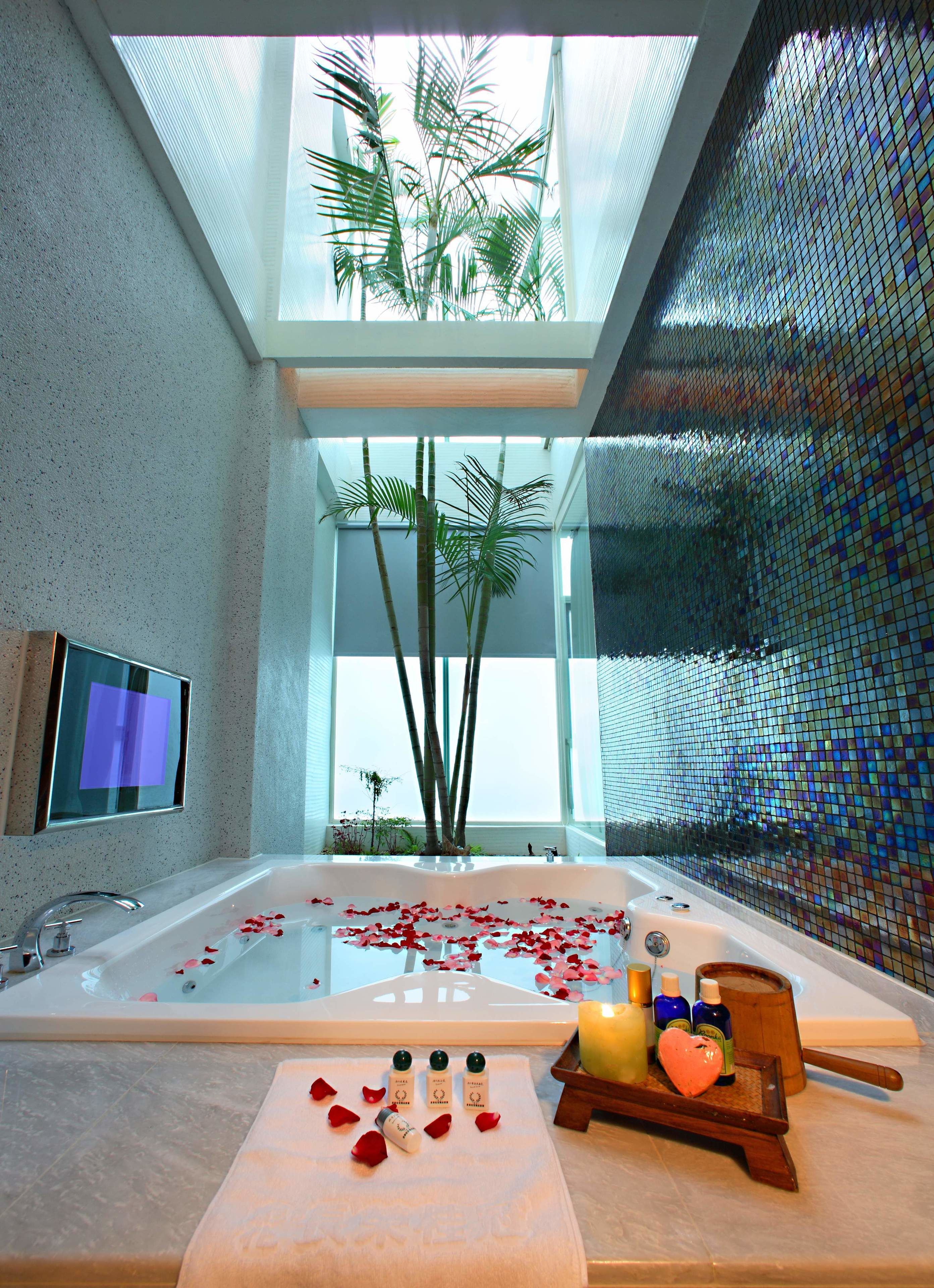 A modern bathroom with a large bathtub, a television mounted on the wall, and a decorative mosaic wall.