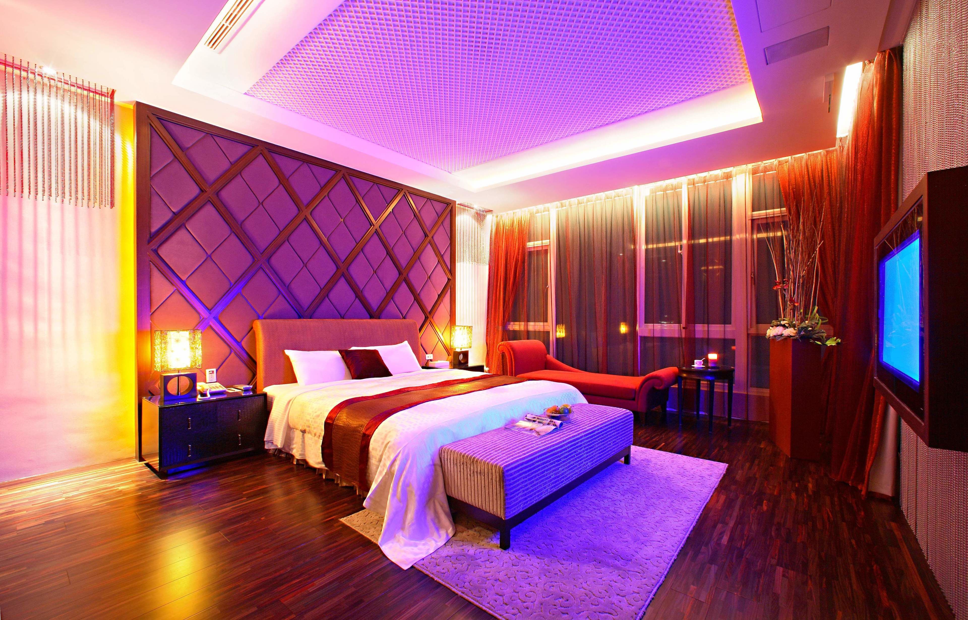 A modern hotel room with a large bed, a desk, a TV, and a window with curtains.