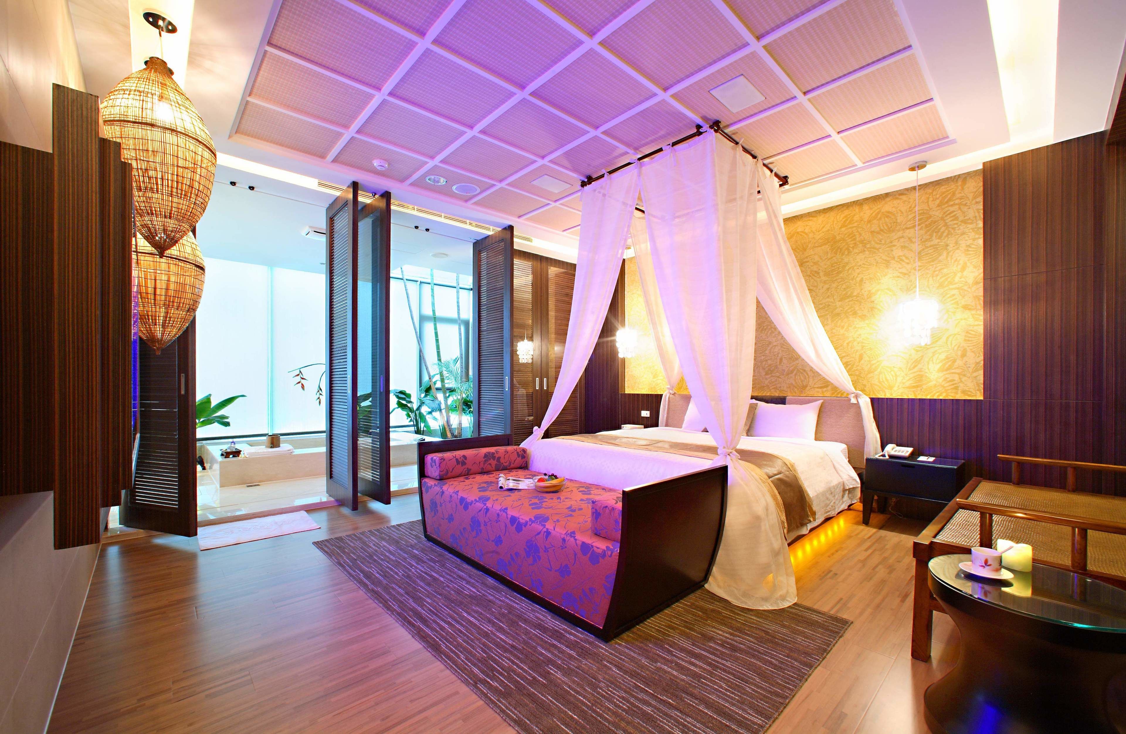 A modern hotel room with a large bed, a sitting area, a small table, and a view of the outdoors.